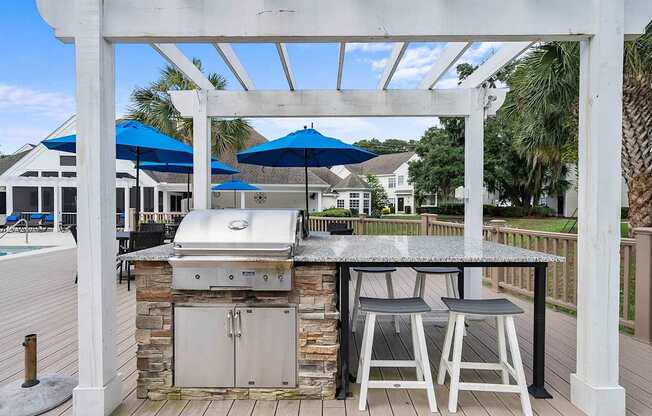 A white pergola with a grill and two chairs under it.