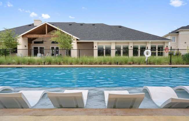 a swimming pool with chairs in front of a house