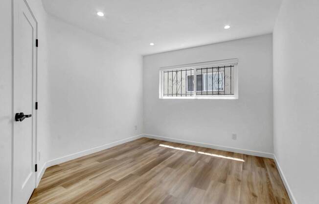 a living room with white walls and wooden floors and a window