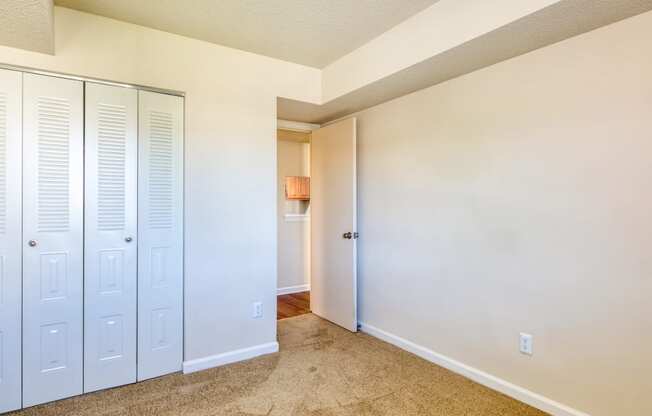 an empty bedroom with white closets and a hallway to a bathroom