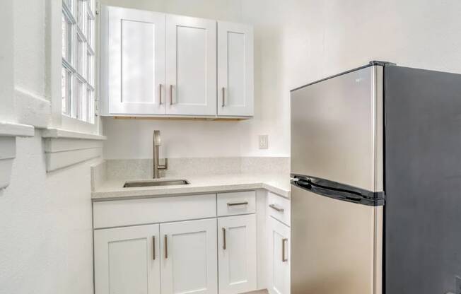 A black refrigerator sits next to a sink in a kitchen with white cabinets.