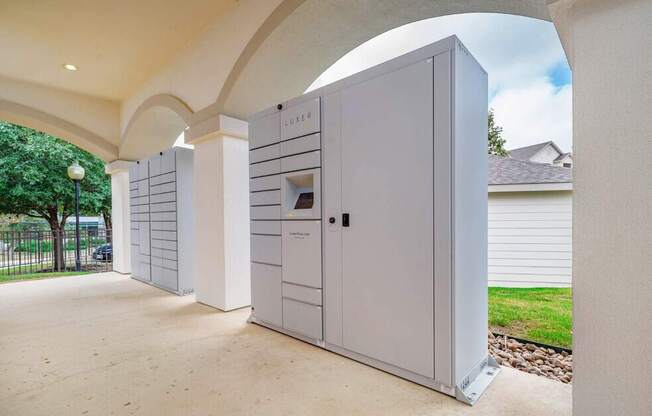 A row of white storage units are lined up in a sunny courtyard.