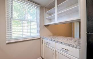 A kitchen with white cabinets and a window with blinds.