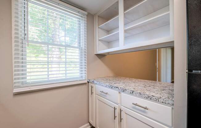 A kitchen with white cabinets and a window with blinds.