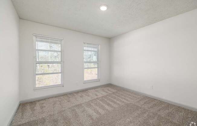 A room with two windows and carpeted floor.