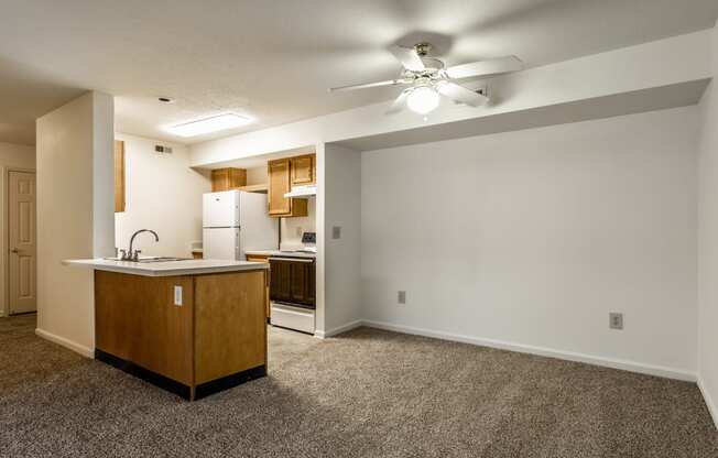 an empty living room with a kitchen and a ceiling fan at Pheasant Run in Lafayette, IN 47909