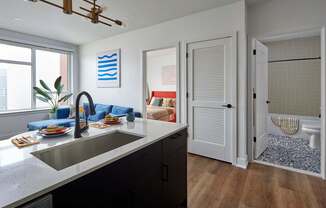 A modern kitchen with a sink, a window, and a view of a living room.