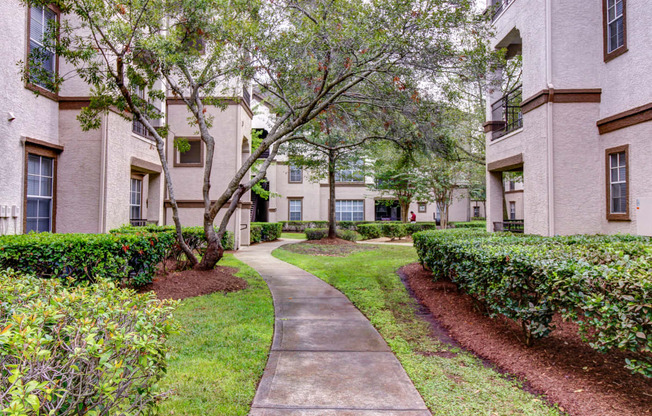 a sidewalk leading to an apartment building with trees and bushes