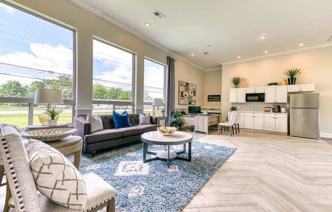 A well-lit, spacious living room with a grey sofa, a round coffee table, and a large window.