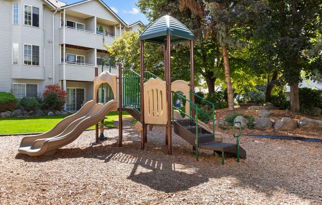 a playground with a slide and a swing set in front of an apartment building