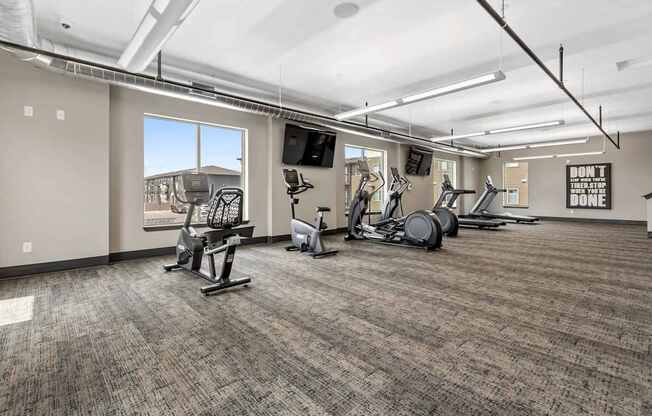 A gym with a variety of exercise equipment and a motivational poster on the wall.
