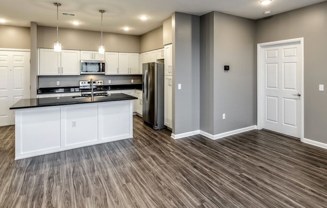 Large living area with kitchen island and white cabinets at The Apartments at Lux 96 in Papillion, NE