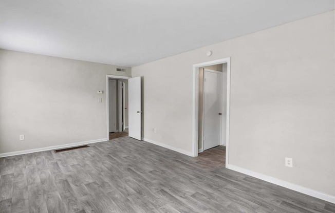 the living room of an apartment with white walls and wood flooring