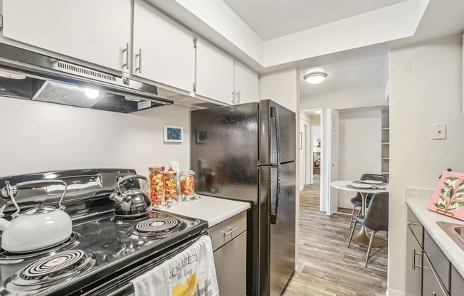 A kitchen with a black refrigerator and a stove with a kettle on it.