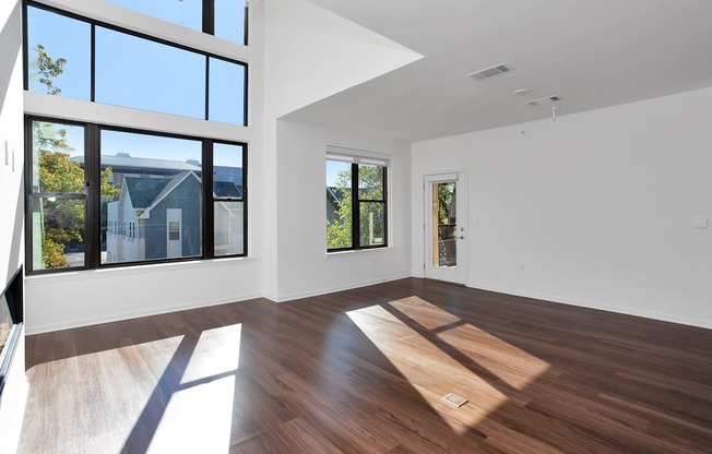 a living room with white walls and wood floors and large windows