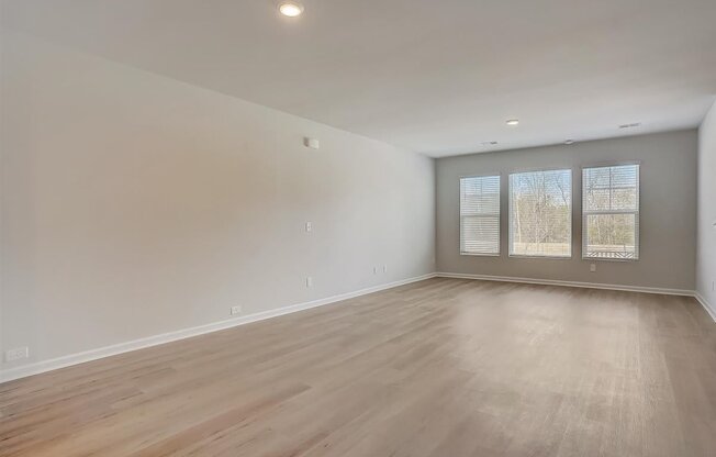 A spacious room with wooden flooring and a window with blinds.