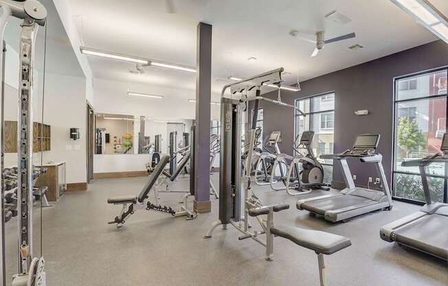 A spacious gym with a variety of equipment including treadmills, weight machines, and a bench press at Infinity on the Point Apartments, Texas