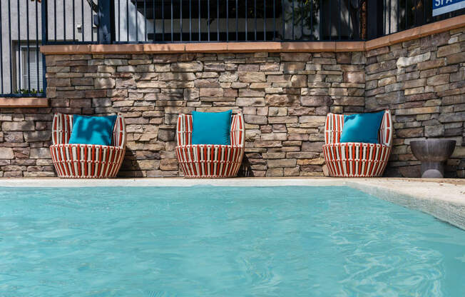 three beach chairs with blue cushions by a swimming pool