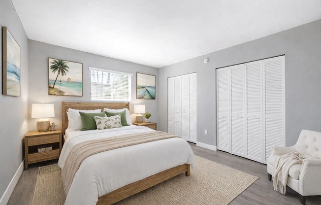A bedroom with a large bed, a nightstand with lamps, a chair, and pictures on the wall.