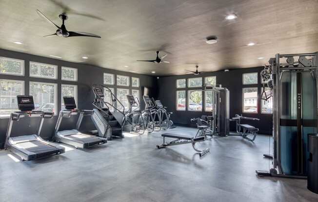 a large fitness room with cardio equipment and windows