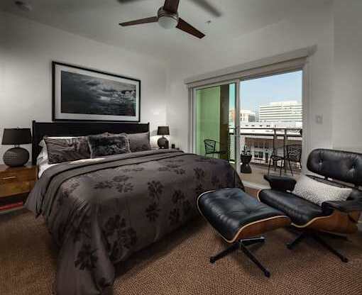 A bedroom with a bed, chair, and ceiling fan.