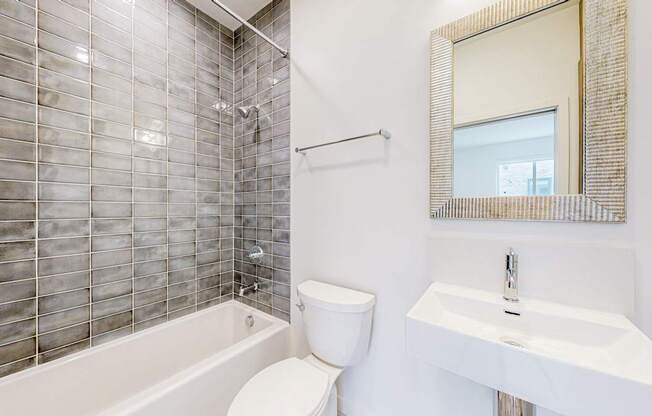 A white toilet sits next to a white sink in a bathroom with a glass block wall at One West Drive Apartments, Excelsior, MN 55331