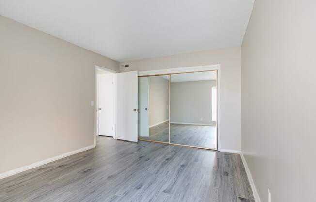 an empty living room with wood floors and a mirrored closet