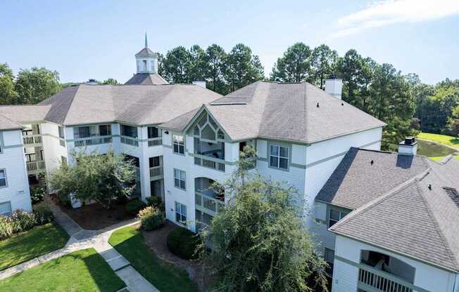 A large white building with a tower and a balcony overlooks a green lawn.