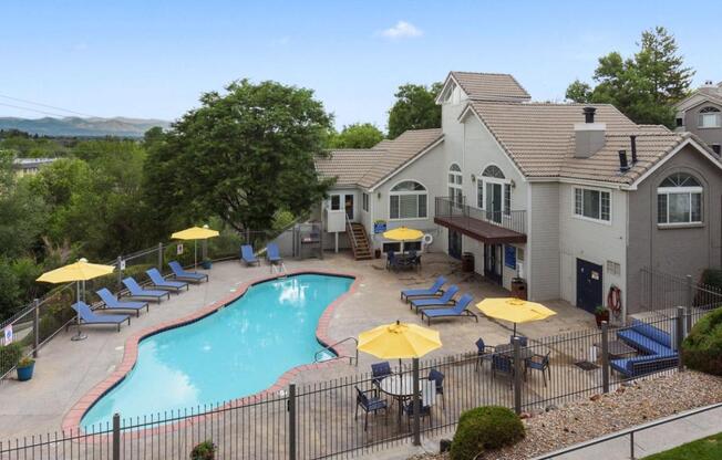 A pool surrounded by chairs and umbrellas with a house in the background.