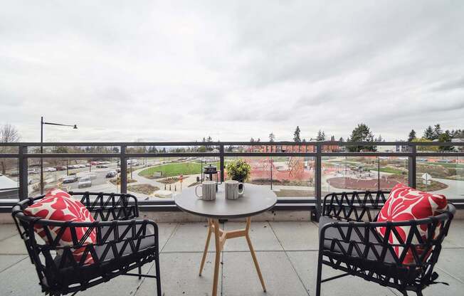 Two chairs and a table with a view of a street and trees.