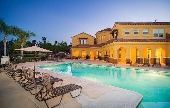 A large swimming pool with lounge chairs and umbrellas in front of a house.
