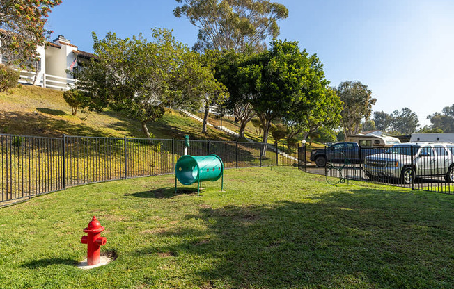 A green barrel sits on a grassy area next to a red fire hydrant.