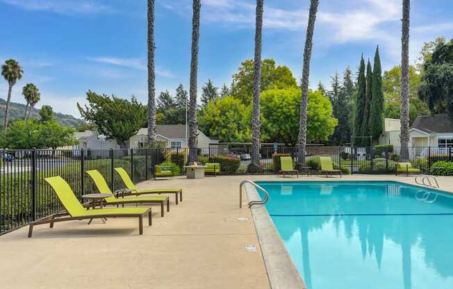 A pool surrounded by palm trees and lounge chairs.
