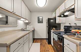 Model kitchen with black appliances, white cabinets, stainless steel sink and vinyl plank flooring at Clackamas Trails Apartments, Oregon, 97222