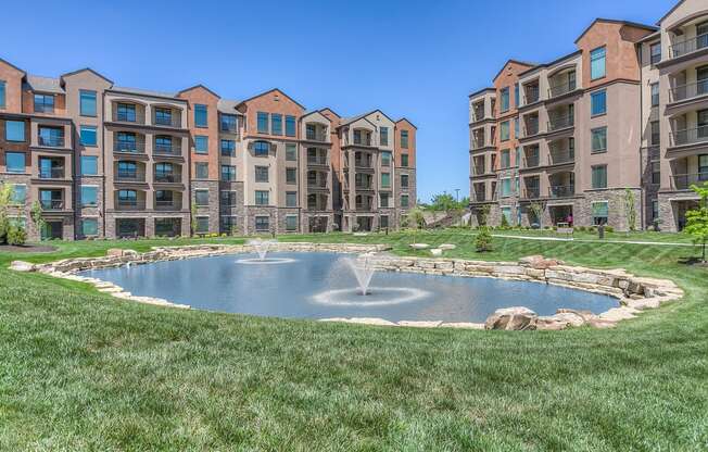 a fountain in the middle of a grassy area with an apartment complex in the background