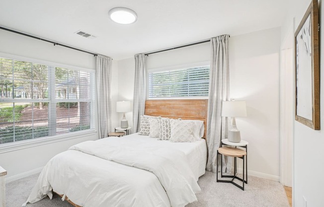 A bedroom with a large bed and a window with white curtains.