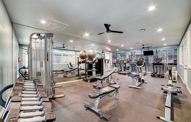 a gym with a lot of exercise equipment and a ceiling fan