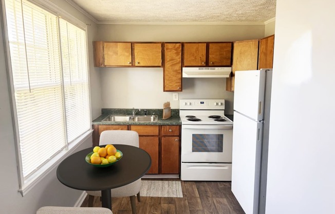 a kitchen with white appliances and a table with a bowl of fruit