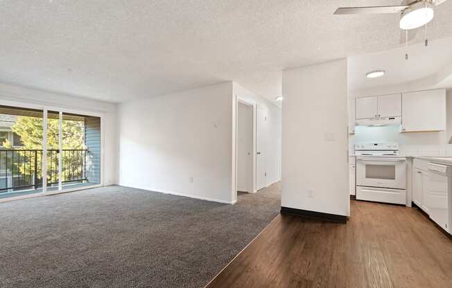 the living room and kitchen of an apartment with white appliances and wood flooring