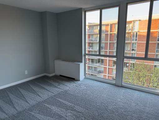 A room with a grey carpet and a large window overlooking a building.