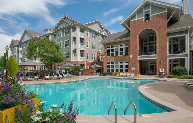 A large swimming pool is surrounded by a yellow planter box with purple and white flowers.