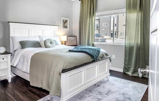 A bedroom with a large bed and a window with green curtains.
