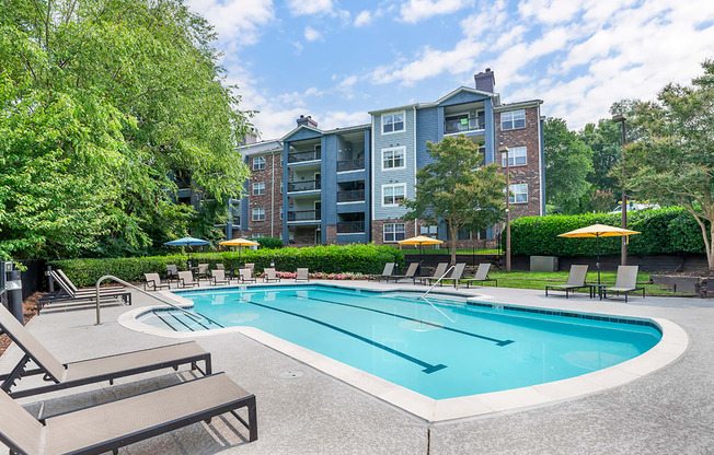 a swimming pool with chairs and umbrellas in front of an apartment building