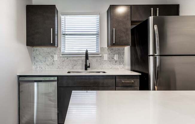 A modern kitchen with a stainless steel refrigerator and a marble backsplash.