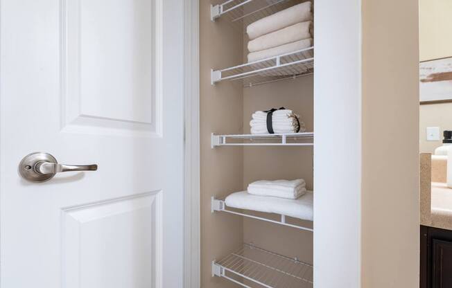 A white door with a silver handle is open to a white shelf with towels on it.