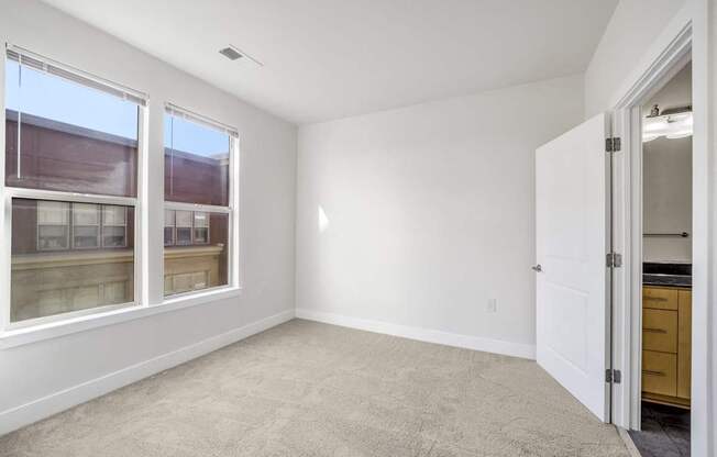 A room with a carpeted floor and a door leading to a kitchen.