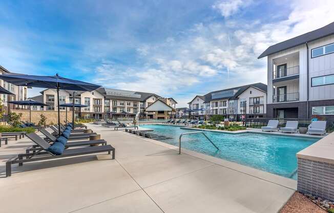 A swimming pool surrounded by sun loungers and umbrellas in a residential area.