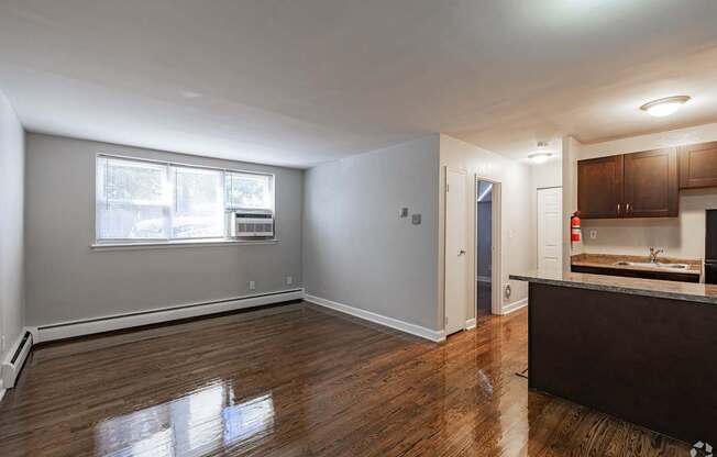 A spacious room with wooden floors and a kitchen area with a sink and cabinets.