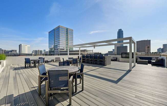 Wooden deck with chairs and a table with a metal frame on the rooftop patio at Dominion Post Oak apartments in Houston, TX