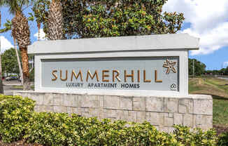 A sign for Summerhill Luxury Apartment Homes is displayed in front of a tree.